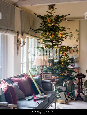 Grand arbre de Noël en coin de salon spacieux avec canapé et panneaux peints chinois ancien. Le canapé d'ameublement et les stores sont de Colefax et Banque D'Images