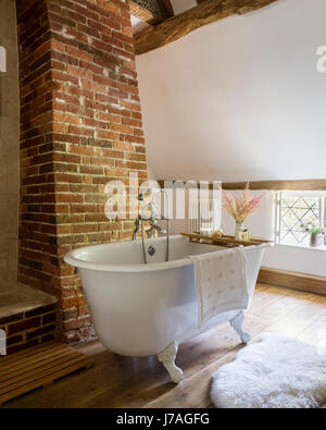 Salle de bains voûtée ancienne avec poutres apparentes, mur en briques apparentes et roll-top de bain français. Banque D'Images