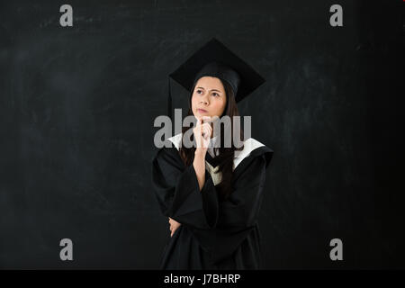 Étudiants diplômés asiatiques pense que son avenir sur fond noir. femme confusion. sa future carrière avec copyspace isolé mur tableau noir. Banque D'Images