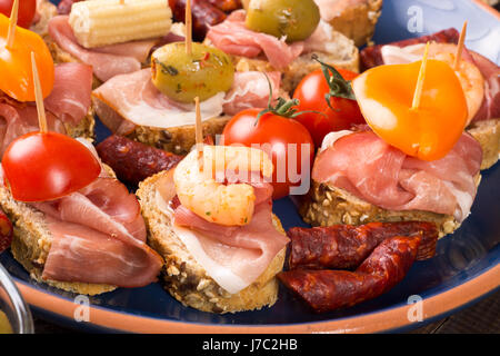 Ensemble de canapés de jambon, olives, tomates et crevettes sur plaque bleue Banque D'Images