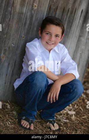 Young Caucasian boy, brune à l'extérieur sur un pied appuyé contre une vieille grange à San Juan Capistrano, en Californie. Banque D'Images