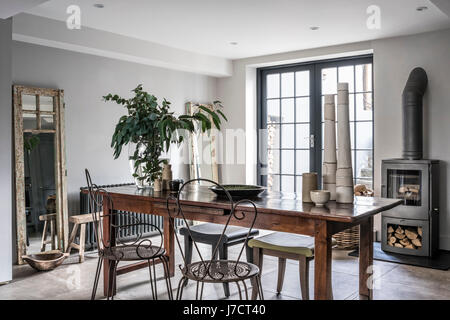 Vintage metal chaises et d'une paire de Philippe Hurel tabourets autour d'une table en bois dans le quartier chic de cuisine avec poêle à bois Banque D'Images