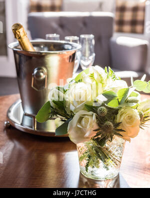 Un posey de roses blanches et de chardons en vase en verre sur la table avec du champagne et de l'argent en arrière-plan de godet Banque D'Images