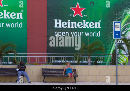 Séparer l'homme et la femme assis sur les bancs de la rue sous deux grands panneaux publicitaires publicité de la bière Heineken Banque D'Images