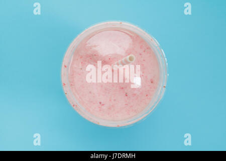 Vue de dessus d'un smoothie aux fraises dans une tasse en plastique avec une paille sur fond bleu. Couleur pastel. L'été et de vie sain concept. Banque D'Images