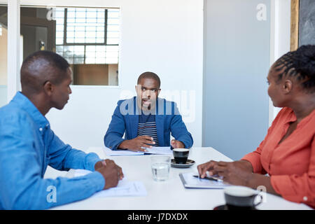 Trois jeunes gens d'affaires de l'Afrique de l'accent assis ensemble dans une réunion à une table dans un bureau moderne discussing paperwork Banque D'Images