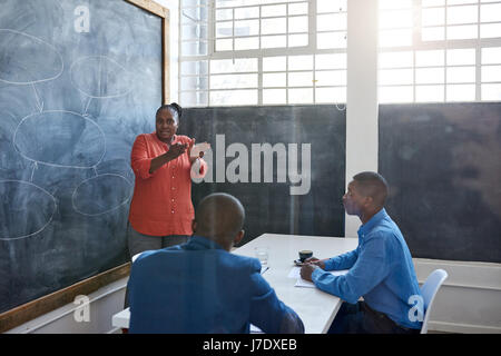 L'accent young African businesswoman donnant une présentation à des collègues alors qu'il se tenait devant un tableau dans un bureau moderne Banque D'Images
