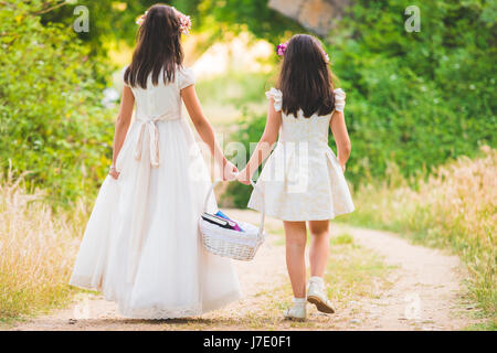 Deux mignonnes petites sœurs marcher sur le terrain et tenant un panier plein de livres Banque D'Images