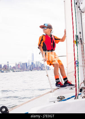 Jeune garçon dans un gilet de holding sur sur un voilier dans la rivière Hudson avec l'île de new york city nyc dans l'arrière-plan Banque D'Images