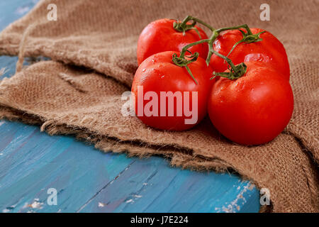 Rouge tomate juteuse photo horizontale branch sur planche de bois bleu. Banque D'Images