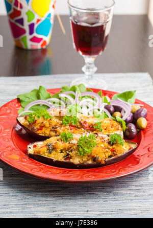 Aubergines farcies au couscous servi avec des feuilles de salade et les olives sur la plaque rouge Banque D'Images