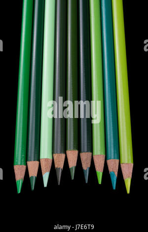 9 crayons vert de différentes teintes et nuances, alignés et isolés contre un fond noir foncé Banque D'Images
