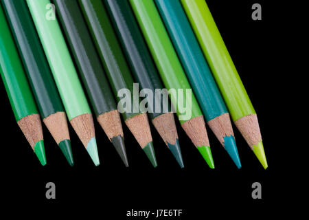 9 crayons vert de différentes teintes et nuances, alignés et isolés contre un fond noir foncé Banque D'Images