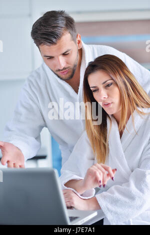 Jeune couple en peignoir à la maison le café dans la cuisine et working on laptop computer Banque D'Images
