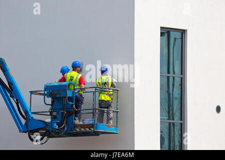 Trois plâtriers sur une grue plâtrer un immeuble de bureaux Banque D'Images