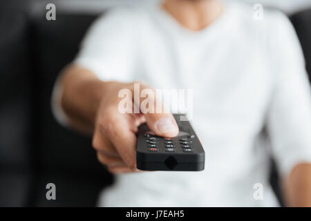 Portrait de jeune homme assis sur le canapé à l'intérieur à la maison tout en maintenant la commande à distance. Banque D'Images