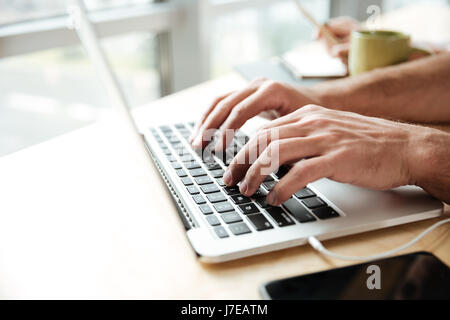 Photo recadrée de jeune homme dans coworking bureau lors de l'utilisation d'un ordinateur portable. Banque D'Images