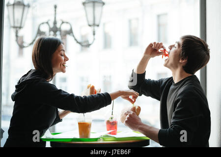 Les jeunes frère et sœur assis dans un café et de manger des hamburgers Banque D'Images