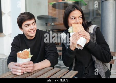 Frère et soeur brune avec des hamburgers assis près de café et à l'écart Banque D'Images