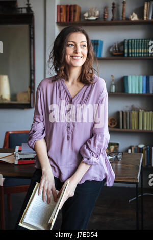 Portrait of a happy smiling mature woman leaning on les 24 et tenant un livre à l'intérieur Banque D'Images