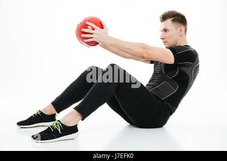 Portrait d'un certain jeune athlète homme faisant des exercices abdominaux avec ballon poids isolated over white background Banque D'Images