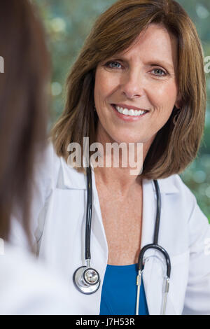 Une happy smiling middle aged female doctor with a stethoscope assis lors d'une réunion avec son collègue dans un bureau de l'hôpital Banque D'Images