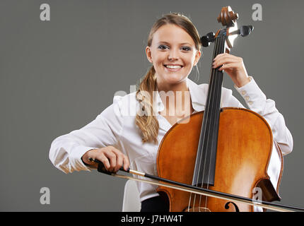 Souriante jeune femme violoncelliste sur fond gris Banque D'Images