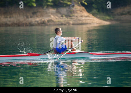 Un jeune concurrent aviron skiff palettes au paisible lac Banque D'Images