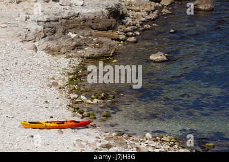 Kayak Orange sur une plage de galets de la côte de la mer à sun summer day Banque D'Images