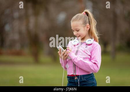 Belle petite fille heureuse d'écouter la musique de smart phone dans le parc. Banque D'Images