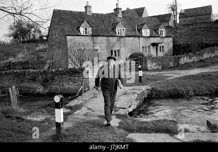 Man la livraison de journaux dimanche matin 1970 UK. La vie du village des Cotswolds. La rivière Eye passerelle. Abattage inférieure et supérieure sont deux villages sur la rivière et l'Œil sont connu comme l'Abat. 1975 HOMER SYKES Banque D'Images