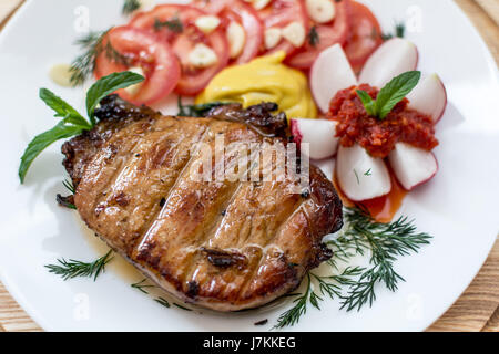 Steak avec des légumes, de l'aneth et l'ail vert, décoré de menthe avec la moutarde et ajika sur une plaque blanche close-up, faible profondeur de champ Banque D'Images