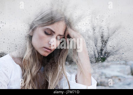 Jeune femme derrière la fenêtre en verre gris sur jour de pluie se sentir triste Banque D'Images