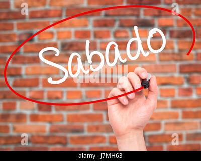 Man main écrit Sabado (samedi en espagnol/portugais) avec marqueur noir sur l'écran visuel. Isolé sur des briques. Le commerce, la technologie, internet concep Banque D'Images