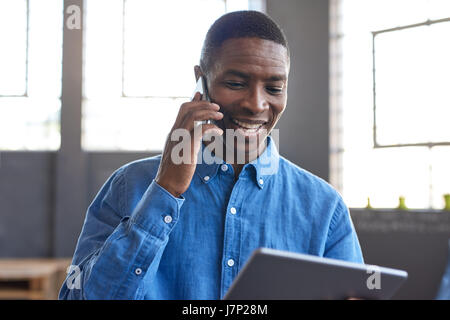 Smiling African businessman using a tablet et téléphone portable au travail Banque D'Images
