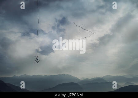 Jeune homme qui tombe du ciel avec une corde attachée à sa jambe comme l'assurance de la sécurité. Base jump, crash, mystérieux et risque la vie difficile détermination concept. Banque D'Images