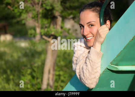 Portrait of a young woman looking at camera, souriant, assis sur un parc diapositive. Banque D'Images
