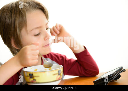 Boy eating céréales et using smartphone Banque D'Images