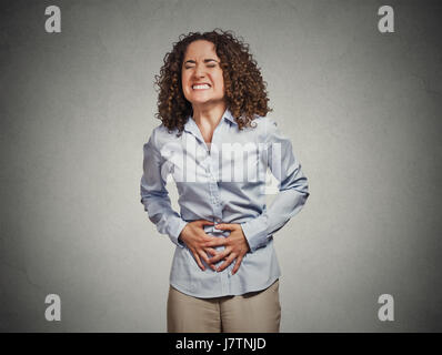 Portrait jeune femme mains sur l'estomac après avoir mauvaise douleur maux gris isolé wall background. L'intoxication alimentaire, la grippe, les crampes. Faciale émotion négative Banque D'Images