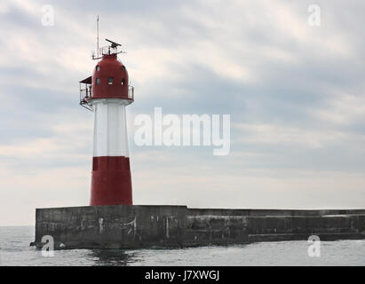 Un phare rouge et blanc en mer. Ciel avec coulds météo sombres. Banque D'Images