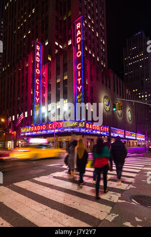 Les personnes qui traversent en direction du Radio City Music Hall de nuit avec Yellow Taxi Cab Driving passé, New York Banque D'Images