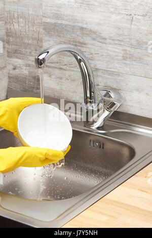 Close up de femmes dans les mains des gants en caoutchouc de protection jaune bol blanc lavage à l'eau courante contre l'évier de cuisine Banque D'Images
