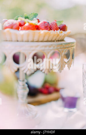 Le côté photo de la partie de l'spondge un gâteau aux fruits couverts de cerises et fraises situé sur le stand blanc gâteau pour Banque D'Images