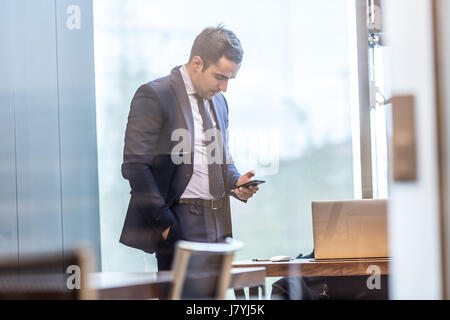 Businessman looking at smart phone in modern bureau d'entreprise. Banque D'Images