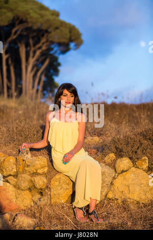 Jeune femme solitaire vêtu d'un CRD d'été jaune assis sur les rochers à l'extérieur pensant Banque D'Images