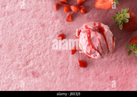 La crème glacée saveur de fraise texture background avec le ballon. Garni de morceaux de fruits et le sirop de fraise. Vue d'en haut. Composition horizontale. Banque D'Images