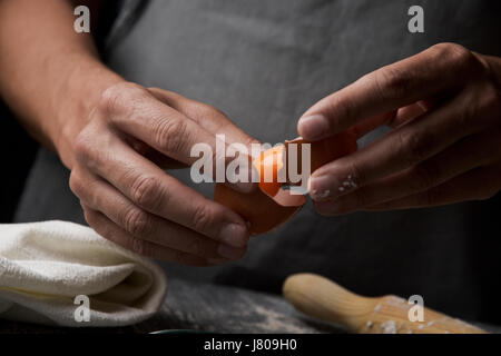 Libre d'un jeune homme de race blanche qui sépare le jaune d'un oeuf à l'aide de la coquille brisée, sur une table en bois rustique à côté d'un rouleau à pâtisserie Banque D'Images