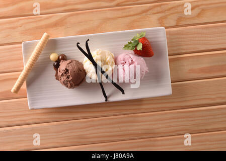 Fraise, Vanille et boules de crème glacée au chocolat blanc sur plaque rectangulaire sur la table en bois. Décoré avec des boules de chocolat, de fruits, de vanille sur branch Banque D'Images