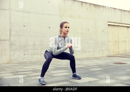 Happy woman doing squats et exerçant à l'extérieur Banque D'Images