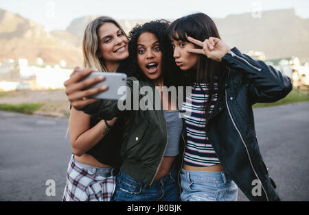 Happy female friends making avec selfies téléphone intelligent. Multi Ethnic groupe de femmes de traîner dans la ville et taking self portrait avec téléphone mobile. Banque D'Images